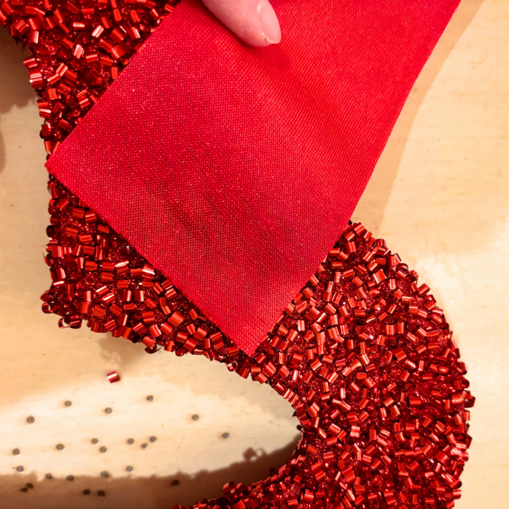 A red velvet ribbon getting glued to the back of a red sparkly heart.